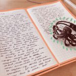 A small notebook is open, with ineligible text written in both. Above the notebook, a cthulhu-shapped metal bracelet (certainly less impressive than the one you are imagining, I'm sorry).